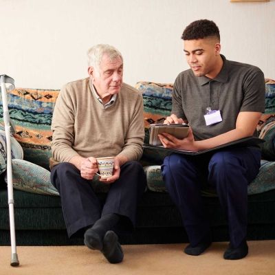Senior man with crutch sitting with young male care worker