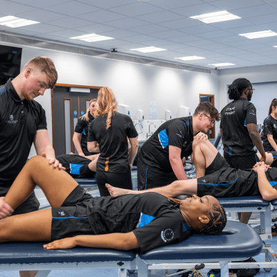 Sports Therapy students in uniform attending to a fellow student laying on a bed