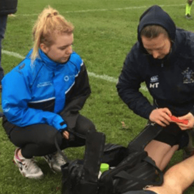 Heather watching a sports therapy attend to a rugby player on the floor