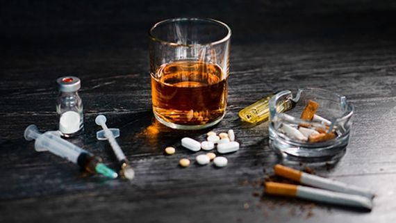 glass of whiskey, ashtray, cigarettes, pills and drug paraphernalia on a table
