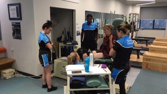 4 Sports therapy students stood around a patient in the human performance lab