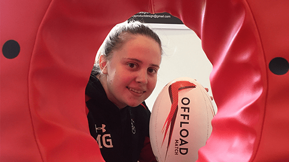 Mandy Grice looking through the rugby tackling pad whilst holding up a rugby ball