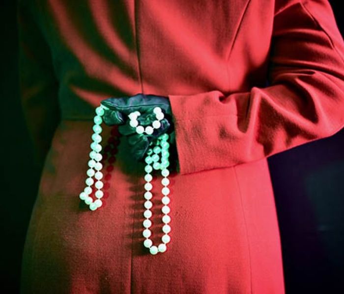 A person in a red coat holding some beads behind their back whilst wearing a black glove