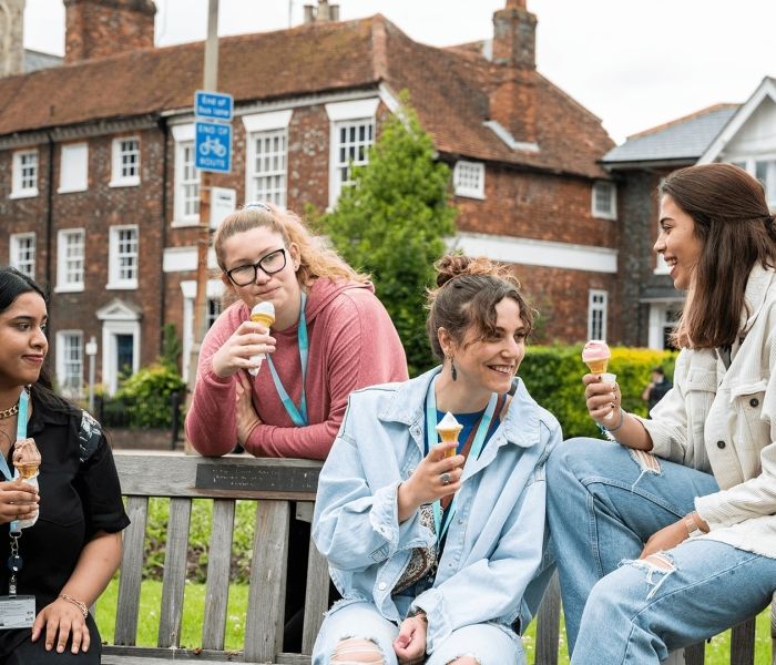 Four female BNU students sat on a bench each with an ice cream in their hand looking at one another and smiling in High Wycombe town centre