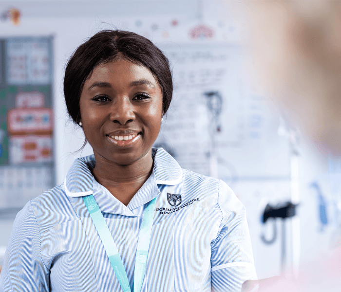 A student nurse in uniform facing the camera and smiling