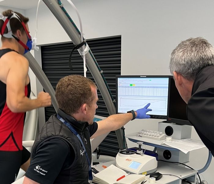 Two lecturers looking at a screen and a student running on a treadmill with an oxygen mask on