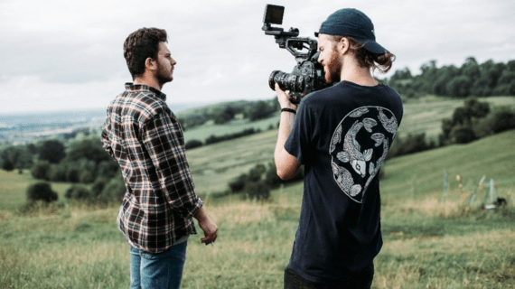 An Acting student stood in a field with a a cameraman by his side.